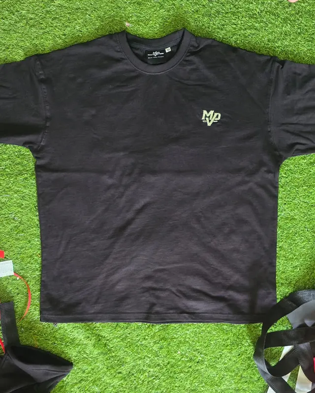 Black oversized tee with a small MVP chest logo on the factory turf backdrop, Wears For You, Sialkot Pakistan
