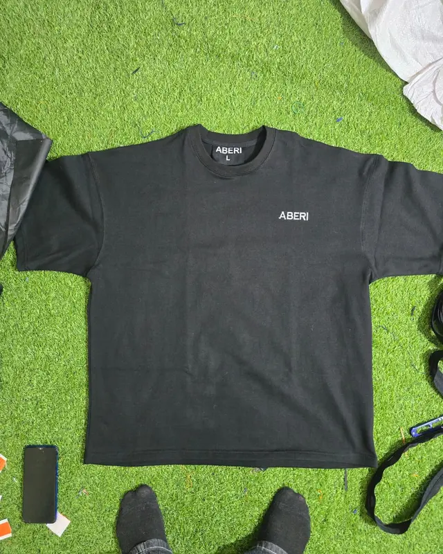 Black oversized tee with a small chest logo on the factory turf backdrop, Wears For You, Sialkot Pakistan